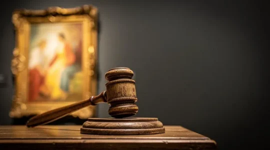 Marteau de commissaire-priseur en gros plan face à une toile floutée en arrière-plan, symbolisant la tension d'une vente aux enchères d'art