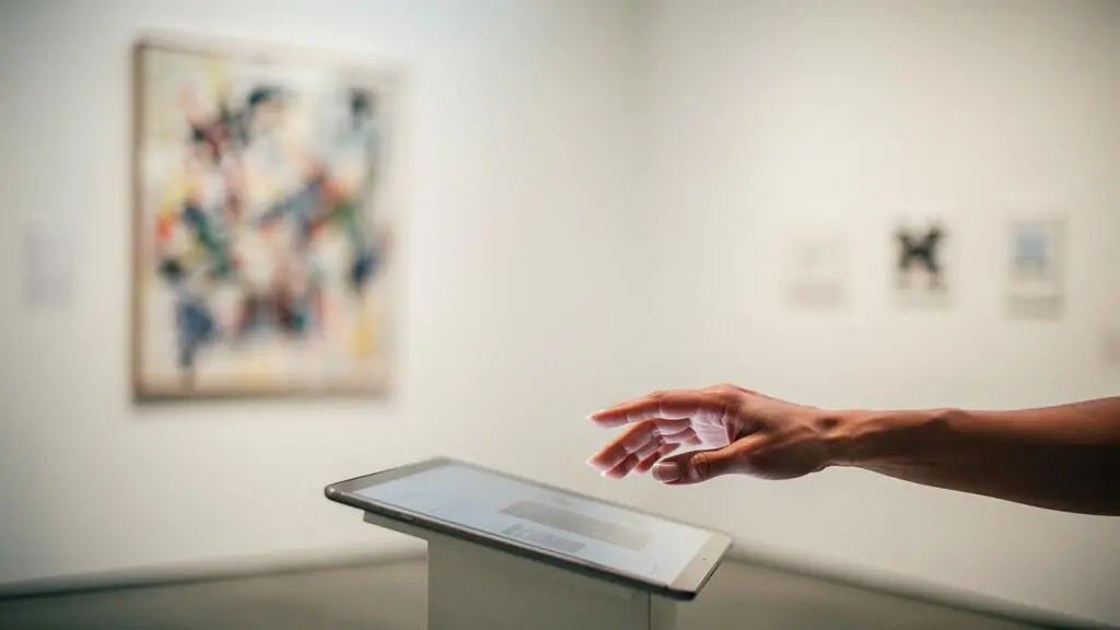 Une main effleurant une tablette affichant une œuvre abstraite face à un mur de galerie vide, symbolisant la rencontre entre l'art physique et le marché numérique