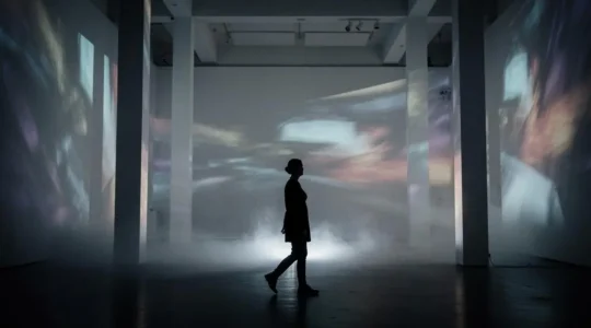 Silhouette d'un visiteur traversant une installation immersive plongée dans la lumière projetée et la brume, mêlant vidéo, son et scénographie